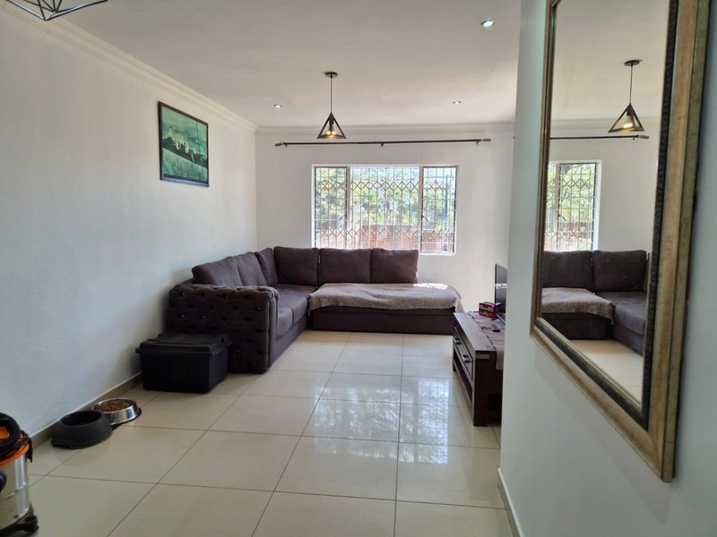 A well-maintained living room featuring large format floor tiles, recessed downlighting, and security bars on the windows, providing a clean and functional living space.