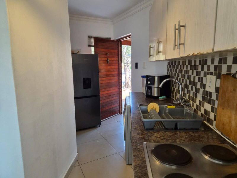 Compact kitchen featuring laminate cabinetry, mosaic tile backsplash, electric hob, and tiled flooring, with direct access to the exterior entrance.