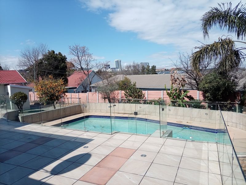 Outdoor pool area featuring a tiled patio, glass balustrade fencing, and a swimming pool with views of the surrounding neighborhood.