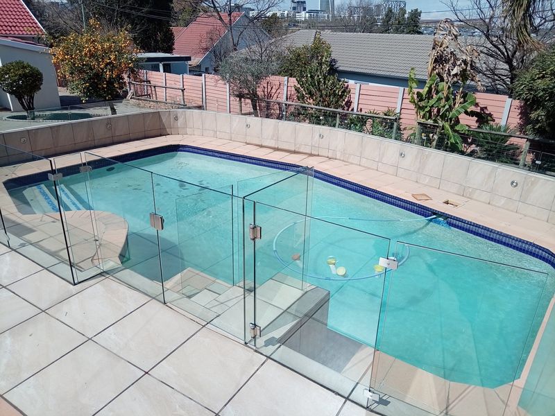 An elevated view of a swimming pool featuring modern glass fencing and tiled surround, set within a private backyard area.