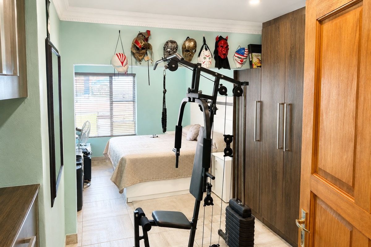 A bedroom featuring built-in cupboards, tiled flooring, and recessed lighting, currently utilized as a multi-purpose space with a home gym setup.