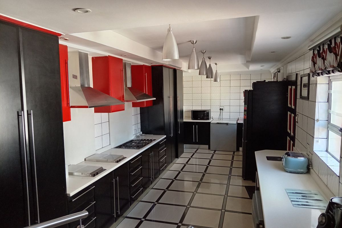 Modern galley-style kitchen featuring high-contrast black and red cabinetry, stone countertops, gas hob, extractor fans, and tiled flooring with recessed lighting.