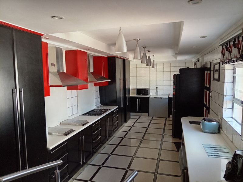 Modern galley-style kitchen featuring high-contrast black and red cabinetry, stone countertops, gas hob, extractor fans, and tiled flooring with recessed lighting.