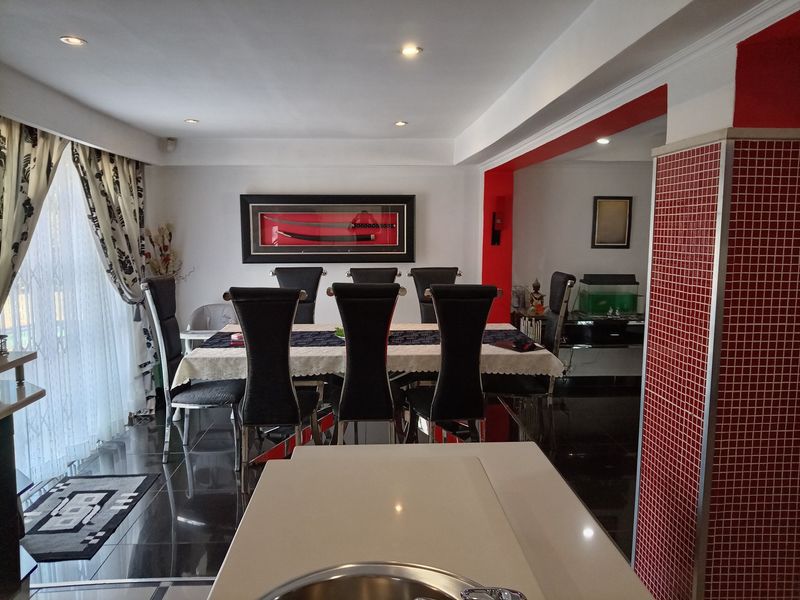 Open plan dining area featuring tiled flooring, recessed lighting, and a distinctive red mosaic tiled pillar, connecting to adjacent living spaces.