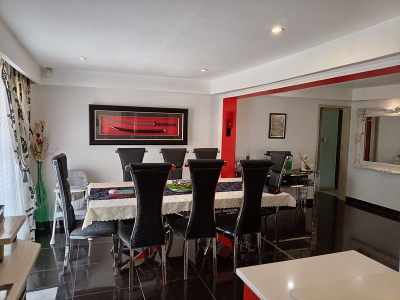 A well-lit dining room featuring polished dark floor tiles and recessed ceiling lighting, creating a clean and functional space for family meals.