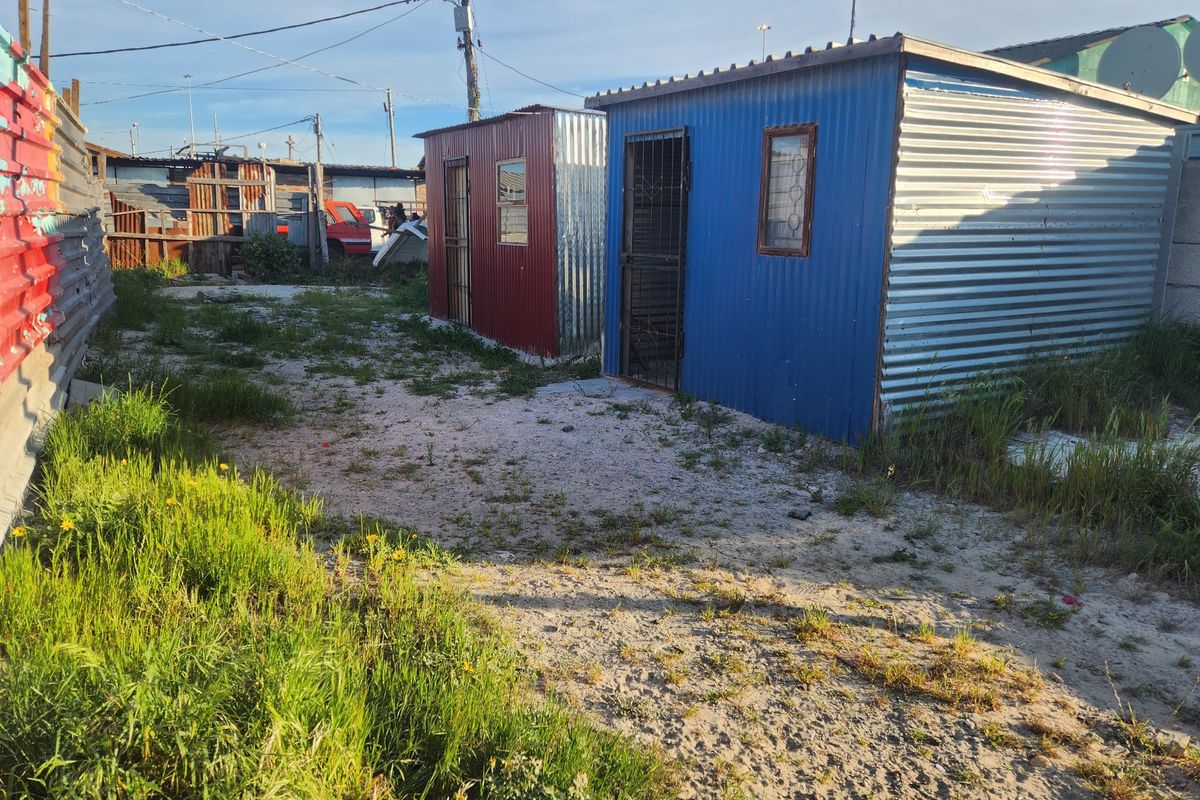 A view of the rear yard featuring two small corrugated metal structures on an unpaved lot with surrounding fencing.