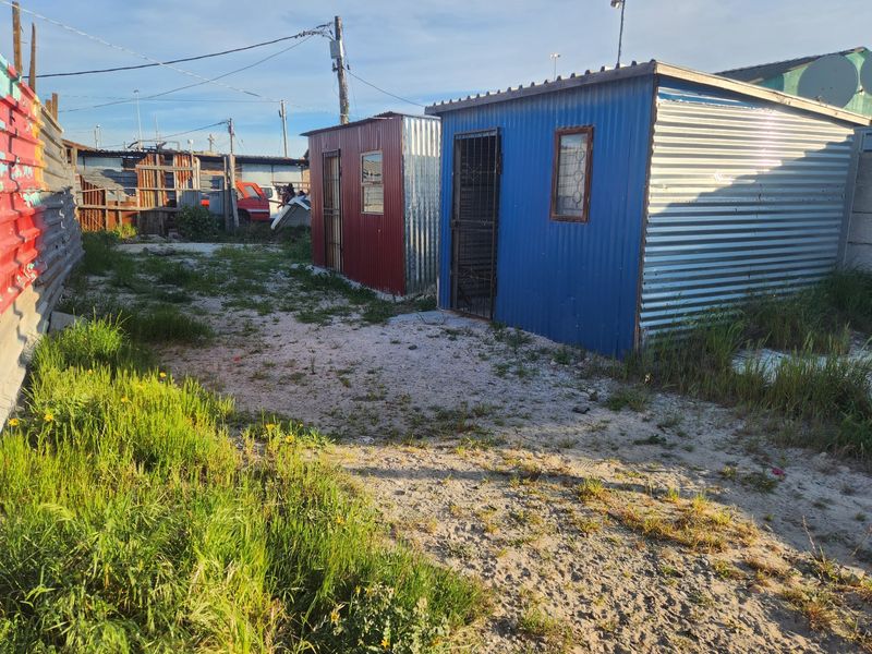 A view of the rear yard featuring two small corrugated metal structures on an unpaved lot with surrounding fencing.