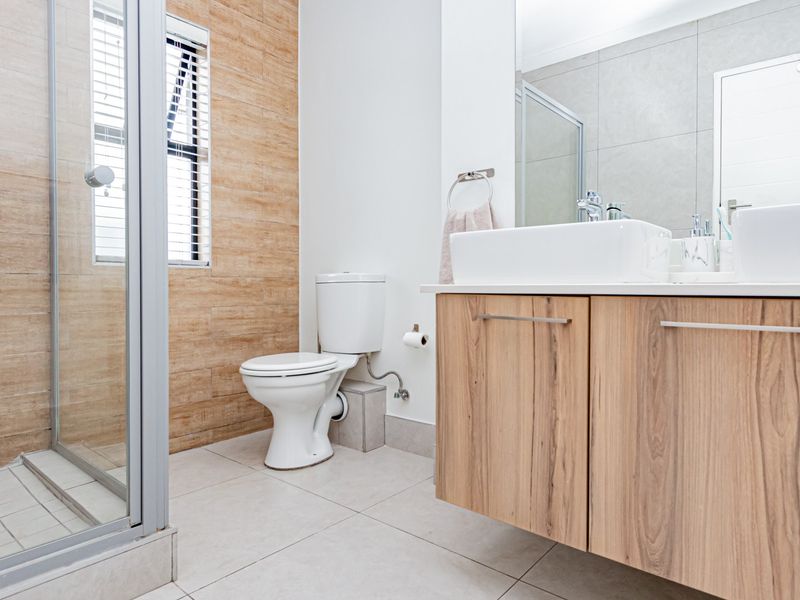 Modern bathroom featuring a floating vanity with dual vessel sinks, a glass-enclosed shower, and contemporary wood-look wall tiling.