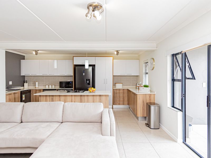 Modern open-plan kitchen and living area featuring a central island, sleek cabinetry, tiled floors, and seamless access to an outdoor patio with a built-in braai.
