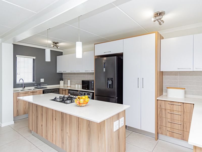 Modern kitchen featuring a central island with gas hob, stone countertops, ample built-in cabinetry, and sleek tiled finishes throughout.