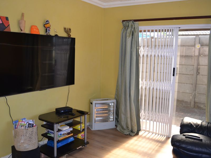 A living room featuring laminate flooring and a sliding glass door with a security gate, providing direct access to the outdoor area.