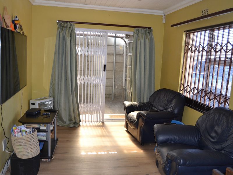 A living room featuring laminate flooring, security bars on windows, and a sliding door leading to an outdoor area.