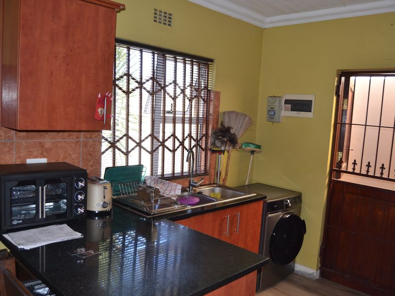 A functional kitchen area featuring granite countertops, built-in cabinetry, a stainless steel sink, and security fixtures on the window and door.