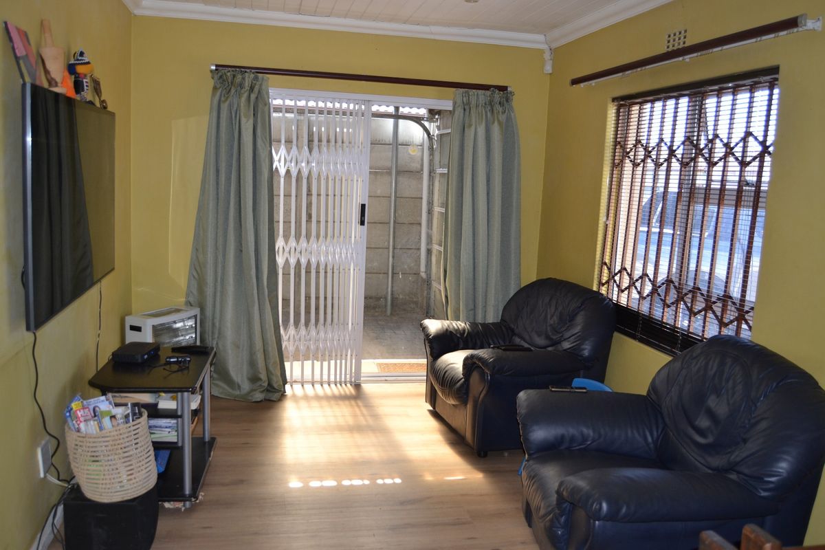A living room featuring laminate flooring, security burglar bars on windows, and a sliding security gate leading to an outdoor area.