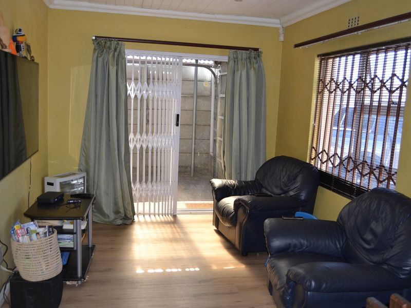 A living room featuring laminate flooring, security burglar bars on windows, and a sliding security gate leading to an outdoor area.