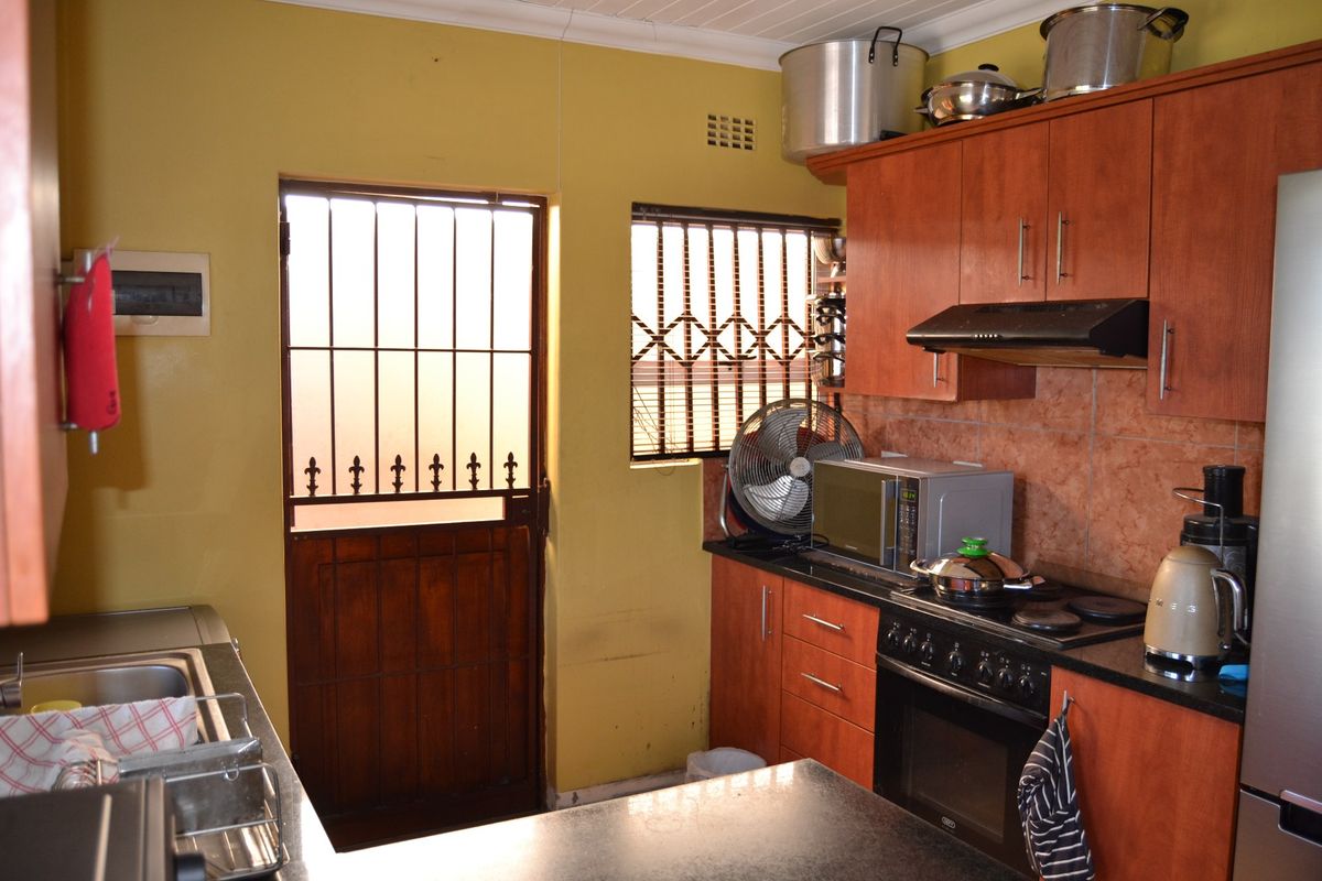 Functional kitchen featuring wood-finish cabinetry, dark countertops, built-in oven with extractor fan, and direct access to the exterior via a security gate.