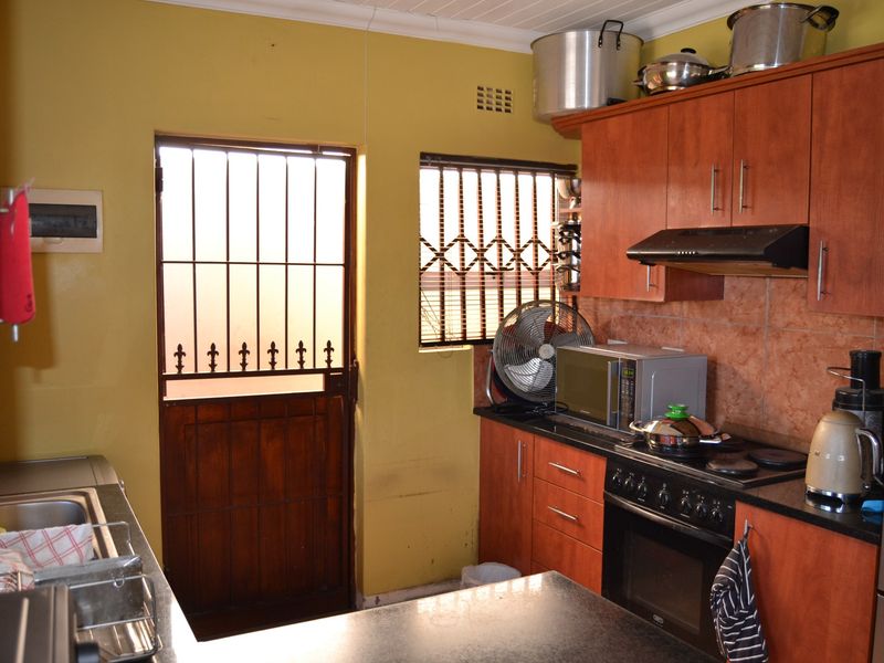 Functional kitchen featuring wood-finish cabinetry, dark countertops, built-in oven with extractor fan, and direct access to the exterior via a security gate.