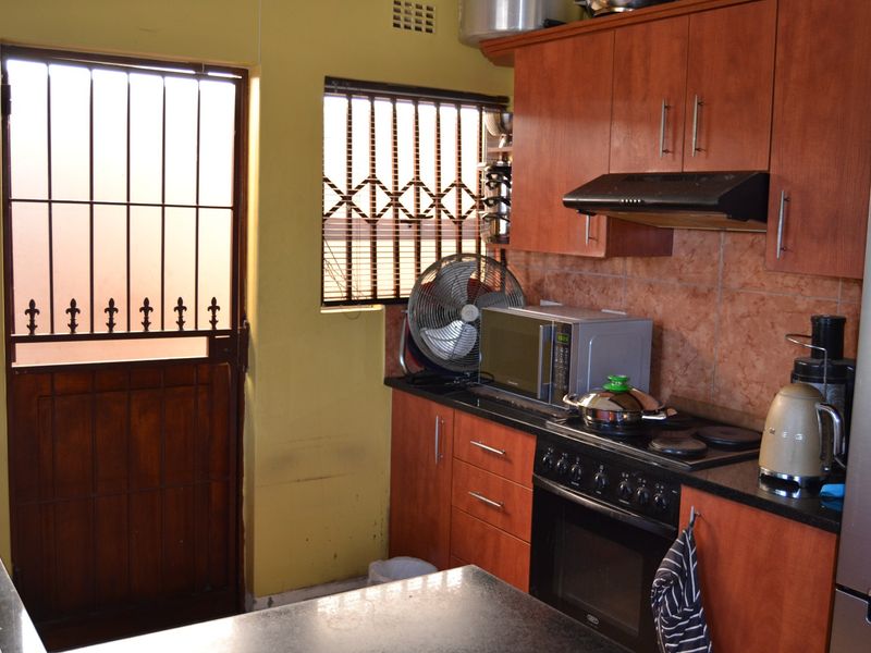 A functional kitchen featuring wooden cabinetry, granite countertops, a built-in oven with hob, and a security gate leading to the exterior.