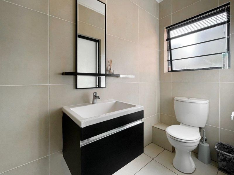 A modern, well-maintained bathroom featuring a wall-mounted vanity with a basin, a sleek mirror, and neutral floor-to-ceiling wall tiles.