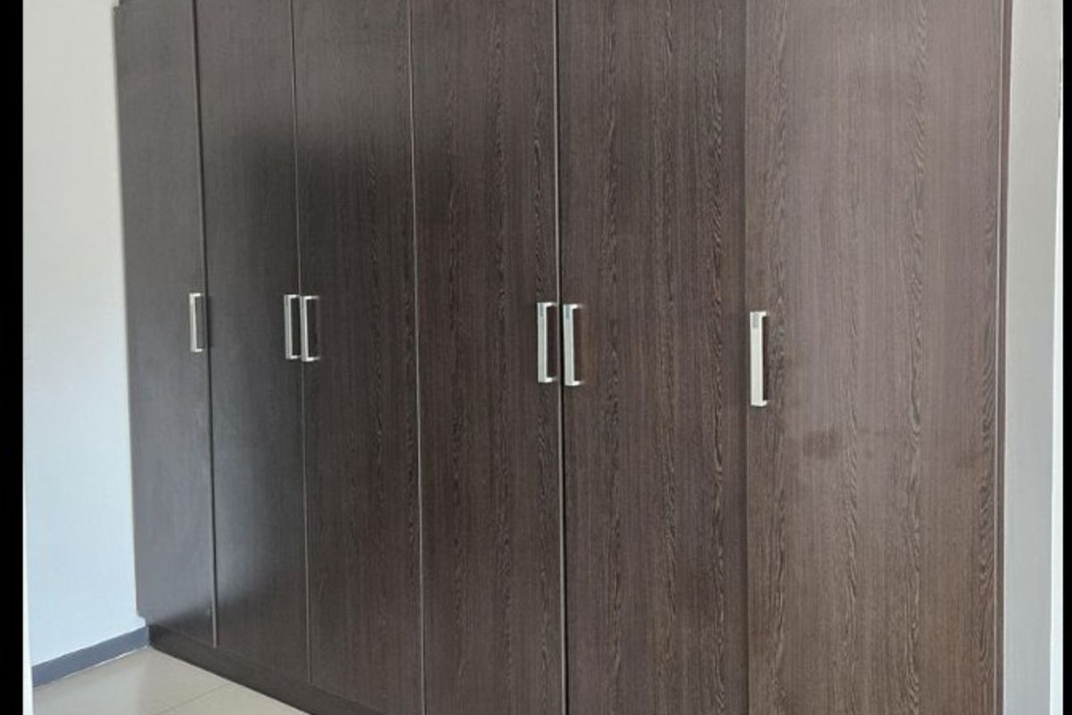 A bedroom featuring extensive dark wood-grain built-in cupboards and neutral floor tiles, providing ample storage space.
