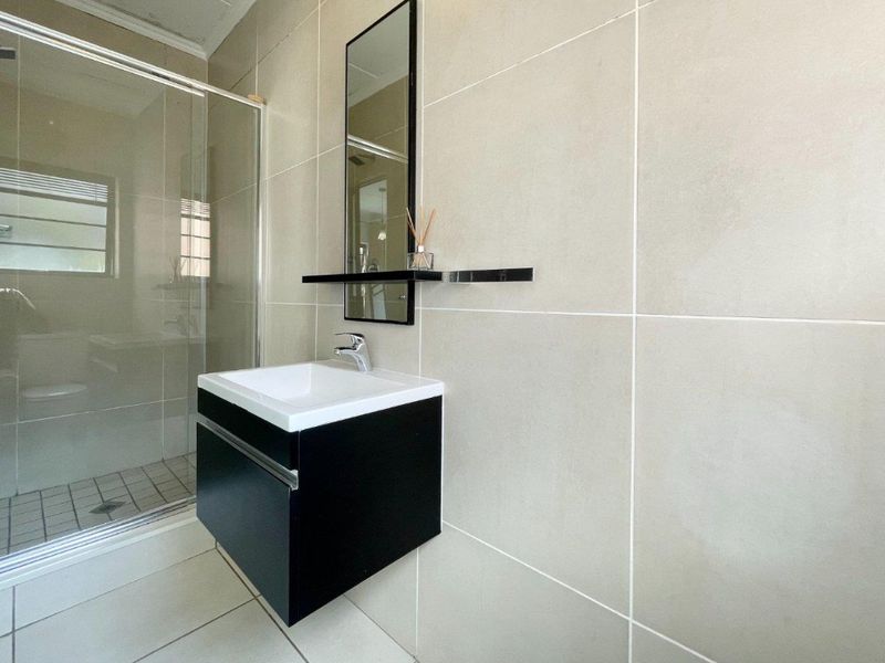 Modern bathroom featuring a wall-mounted vanity, glass shower enclosure, and neutral large-format ceramic wall and floor tiles.