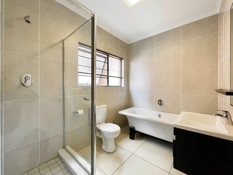 Modern bathroom featuring a walk-in shower with glass enclosure, a freestanding bathtub, wall-mounted vanity basin, and neutral floor-to-ceiling tiling.