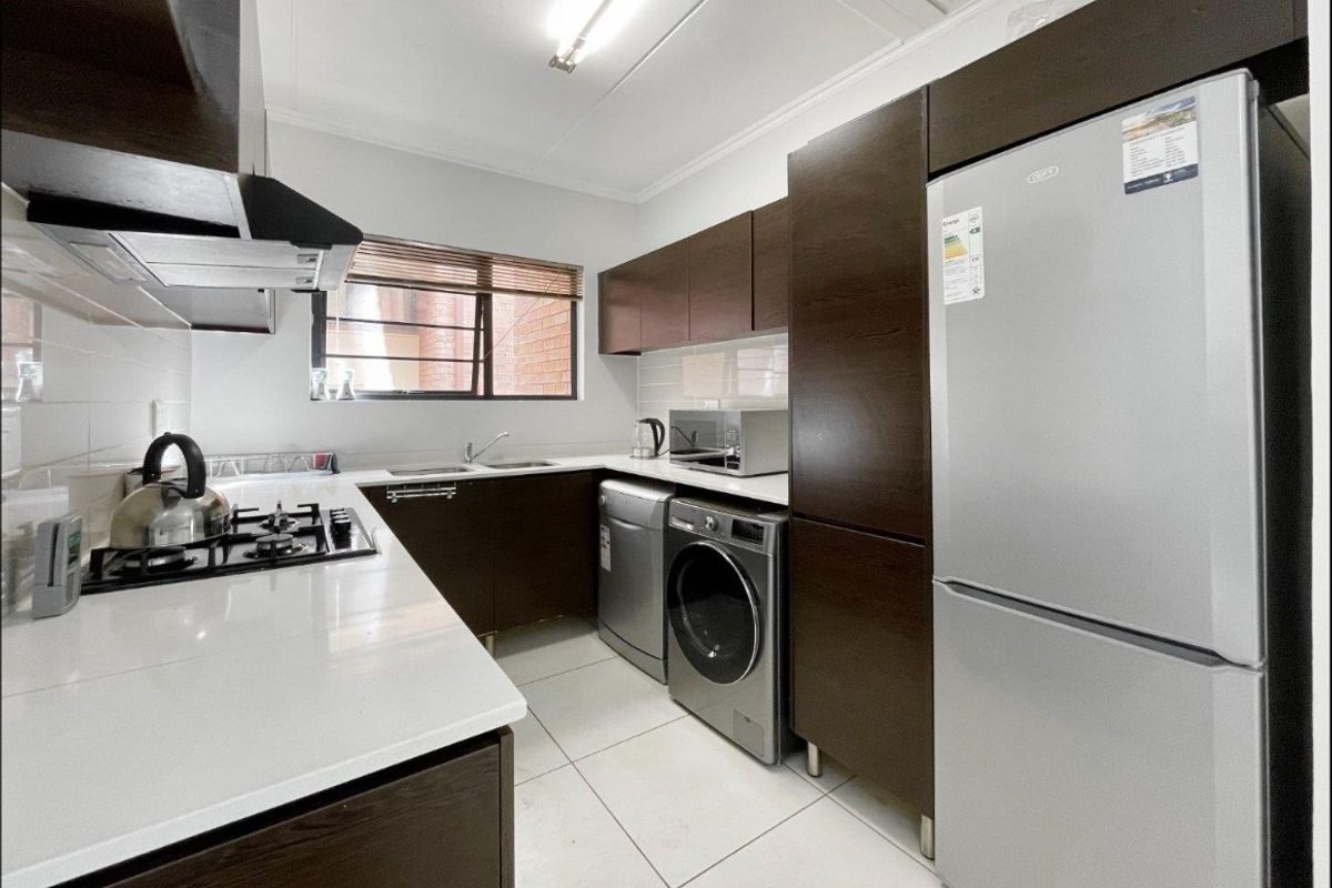 A modern, well-maintained kitchen featuring dark wood cabinetry, white countertops, a gas hob, extractor fan, and tiled flooring with integrated appliance spaces.