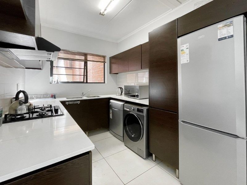 A modern, well-maintained kitchen featuring dark wood cabinetry, white countertops, a gas hob, extractor fan, and tiled flooring with integrated appliance spaces.