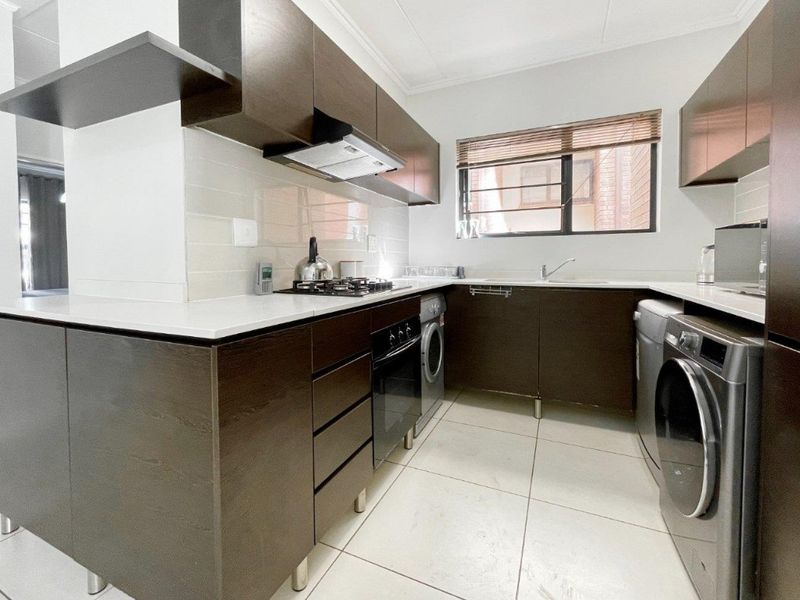 Modern kitchen featuring dark wood cabinetry, stone countertops, gas hob, built-in oven, extractor fan, and tiled flooring with integrated laundry appliance space.