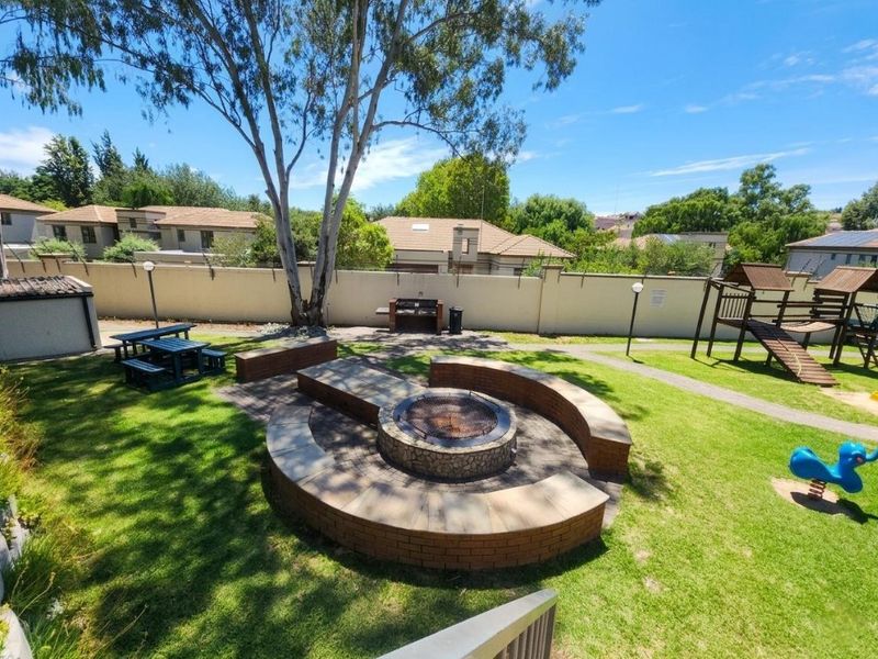 Communal garden area featuring a circular brick fire pit with integrated seating, a built-in braai, and a landscaped lawn.