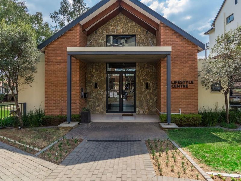 The entrance to the apartment complex lifestyle centre, featuring a brick and stone facade with a covered walkway and landscaped surroundings.