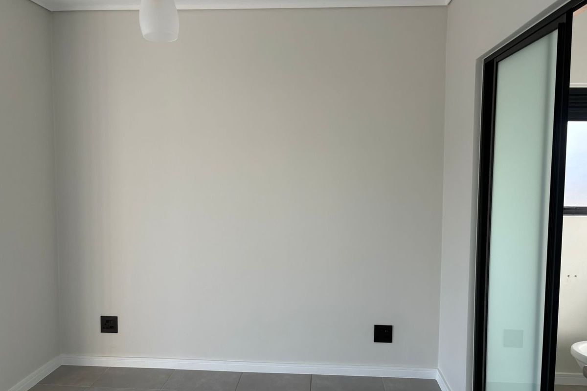 A clean, neutral-toned bedroom featuring tiled flooring, modern electrical fittings, and a sliding door leading to an adjacent space.