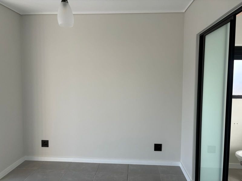 A clean, neutral-toned bedroom featuring tiled flooring, modern electrical fittings, and a sliding door leading to an adjacent space.
