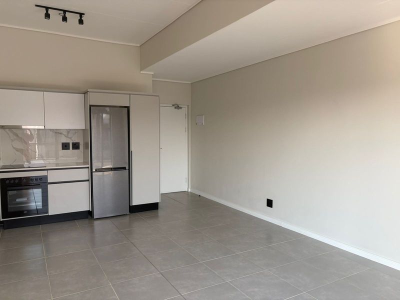 Modern open-plan kitchen area featuring sleek white cabinetry, built-in appliances, and neutral tiled flooring in a clean, well-maintained apartment space.
