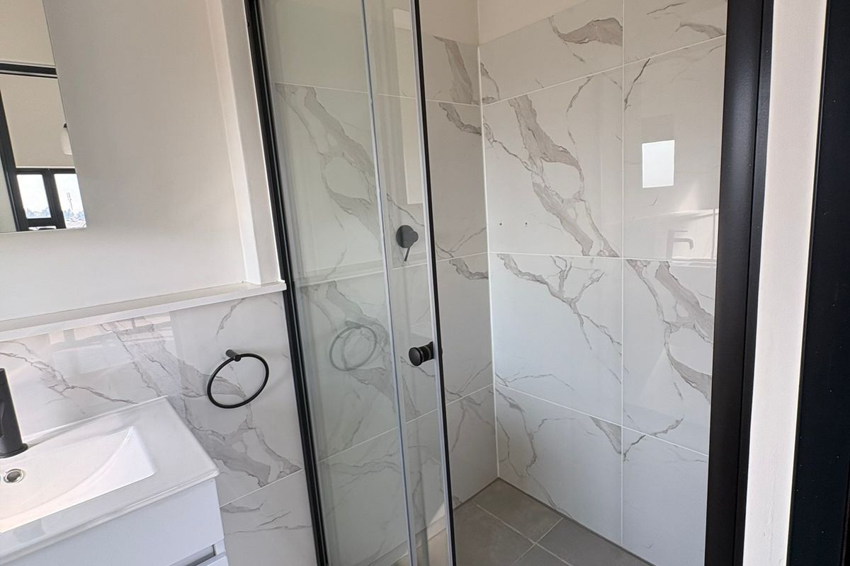 Modern bathroom featuring a walk-in shower with black frame, marble-look wall tiles, and a sleek vanity unit with black tapware.