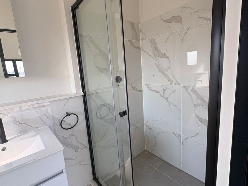 Modern bathroom featuring a walk-in shower with black frame, marble-look wall tiles, and a sleek vanity unit with black tapware.