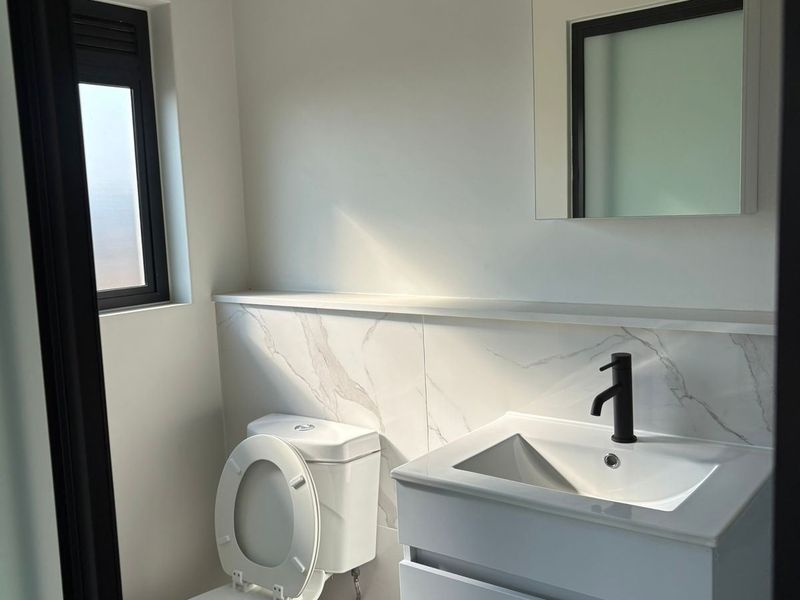 A modern, clean bathroom featuring a wall-mounted vanity with a black mixer tap, a toilet, and a tiled splashback.