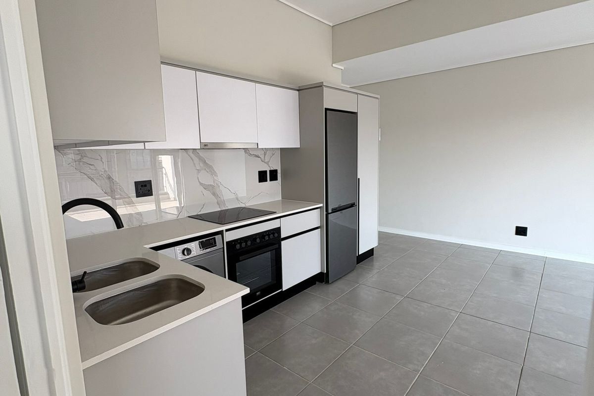 Modern, minimalist kitchen featuring sleek white cabinetry, stone-look backsplash, integrated appliances, and neutral tiled flooring in an open-plan layout.