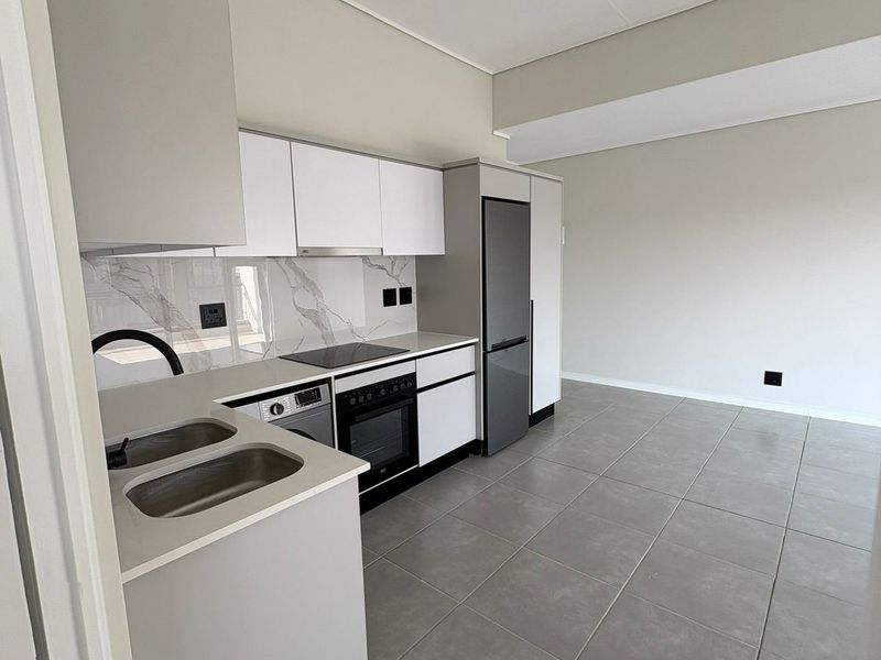 Modern, minimalist kitchen featuring sleek white cabinetry, stone-look backsplash, integrated appliances, and neutral tiled flooring in an open-plan layout.