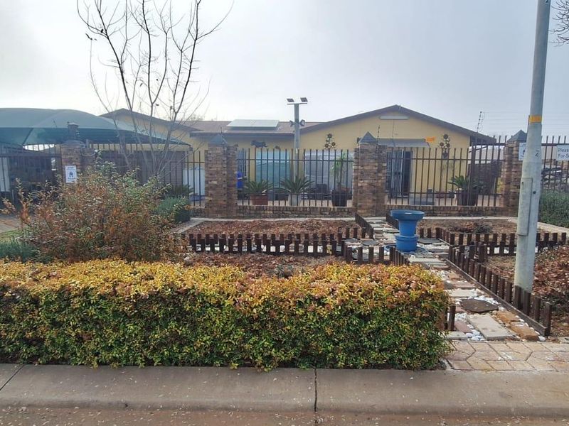 Front view of the property featuring a brick boundary wall, metal security fencing, paved driveway, and a carport.