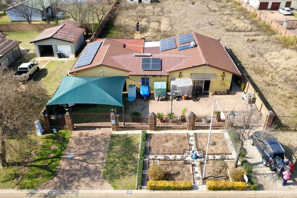 Aerial view of the property featuring a metal roof with installed solar panels, a paved driveway, detached garage, and a shaded outdoor area.