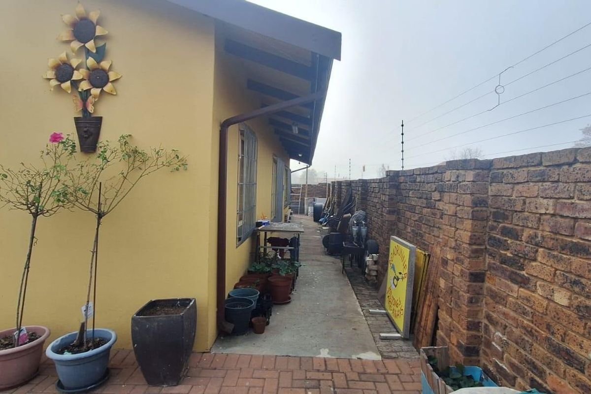 A side exterior view of the property featuring a concrete pathway, brick boundary wall with electric fencing, and a paved patio area.