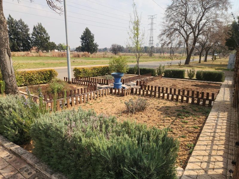A landscaped front garden featuring paved walkways, structured garden beds with timber edging, and established hedging.