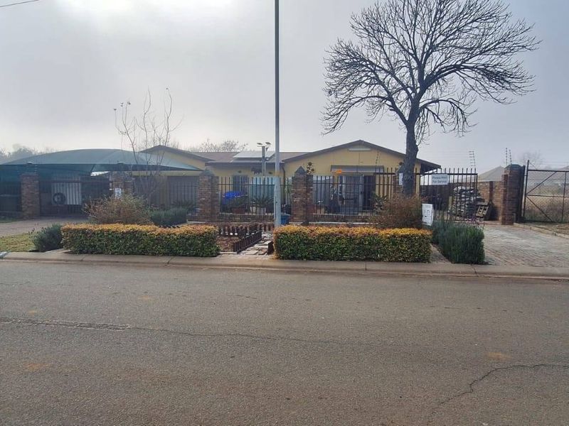 Front view of a residential property featuring a paved driveway, carport, brick perimeter wall with security fencing, and solar panels on the roof.