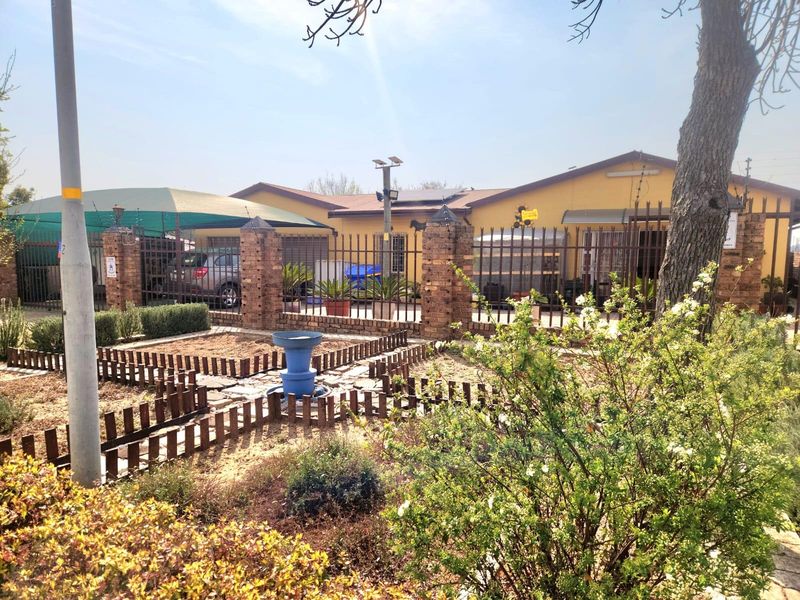 Front view of the property featuring a brick perimeter wall, metal security fencing, a carport, and solar panels installed on the roof.