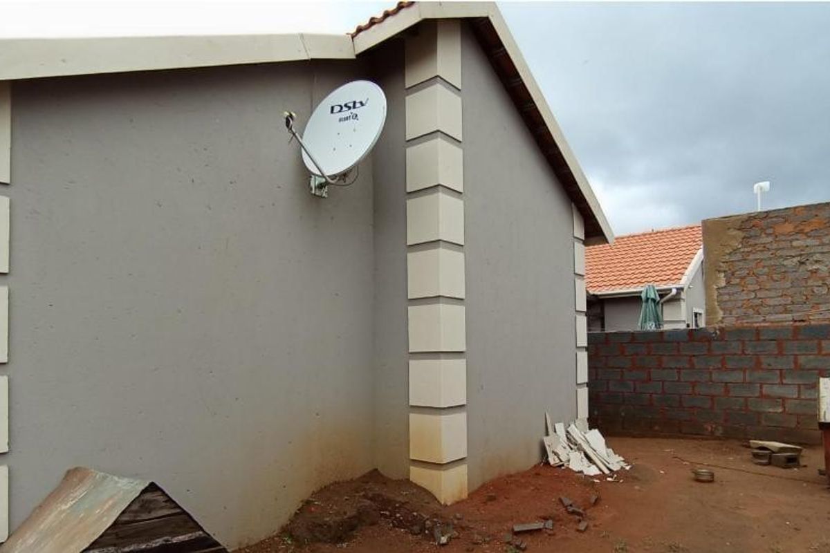 Rear exterior view of the property showing the side facade, satellite dish installation, and an unfinished masonry boundary wall.