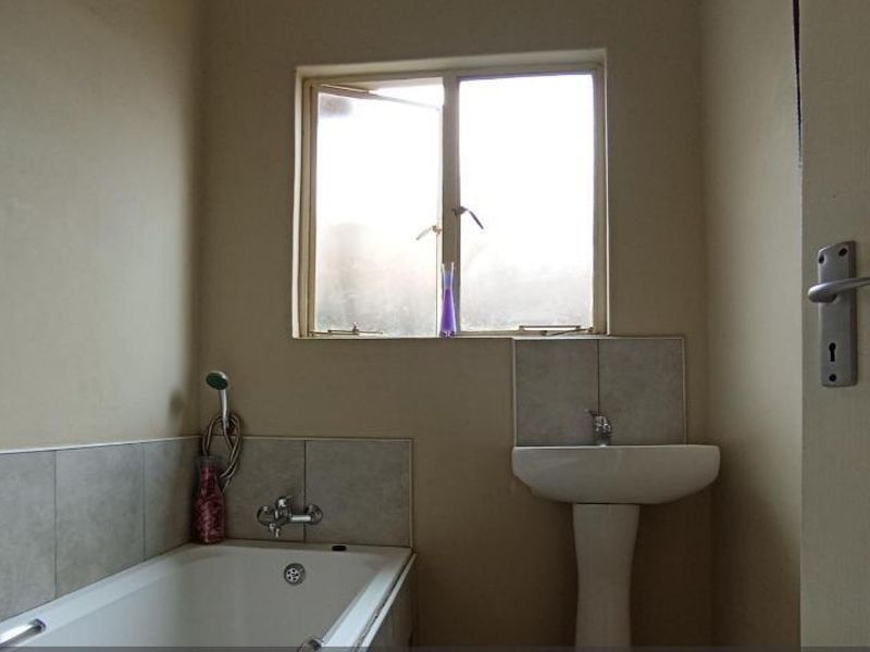A compact bathroom featuring a pedestal basin and a built-in bathtub with tiled splashbacks, requiring cosmetic updates to improve its overall condition.