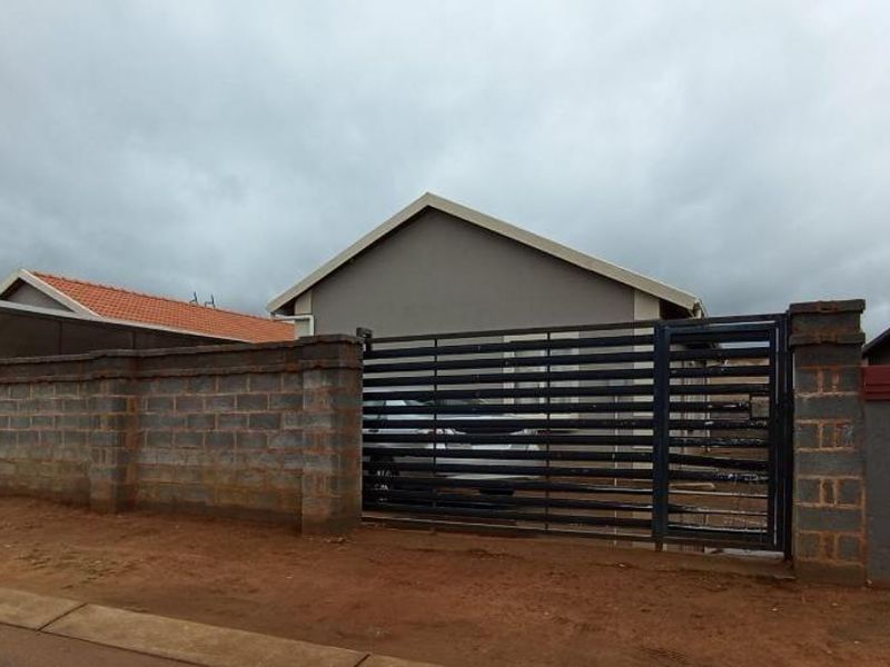 Front view of the property featuring a secure metal gate, perimeter walling, and a tiled roof structure.