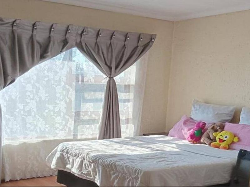 A bedroom featuring laminate flooring and a large window with curtains, providing natural light to the space.
