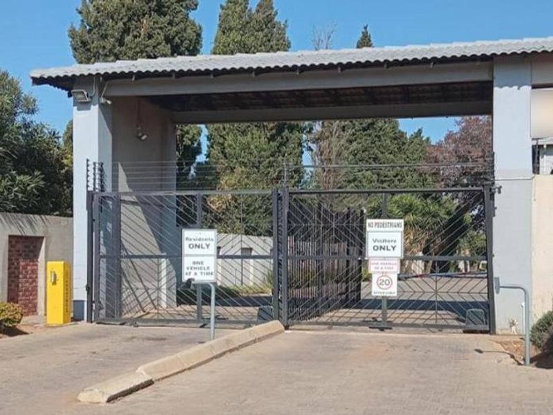 Secure gated entrance to the apartment complex featuring automated vehicle access control, electric fencing, and a dedicated guard house.